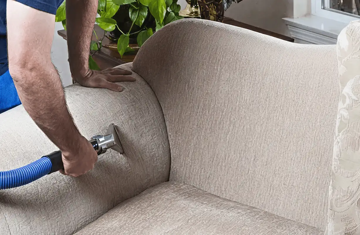 Professional upholstery cleaner deep-cleaning a fabric sofa with a handheld extraction tool and hose, Tucson, AZ.